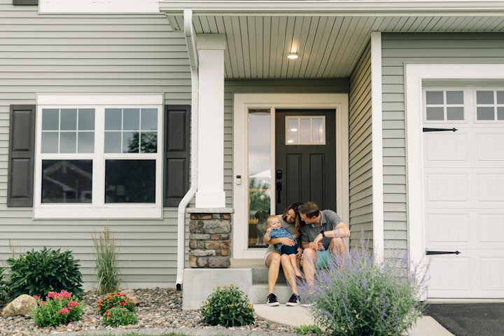Two people sitting together on the front steps of a gray house